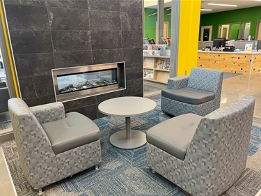 Fireplace and chairs in lobby with the library and recreation front desk in the background.