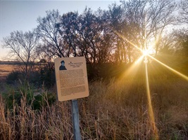 A sign honoring the memory of Frank Shoemaker marks the trail head. The setting sun sets golden rays of light through the trees silhouette.