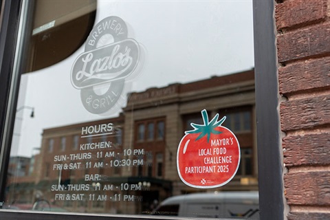A Mayor's Local Food Challenge Particpant 2025 sticker on a window at Lazlo's restaurant.
