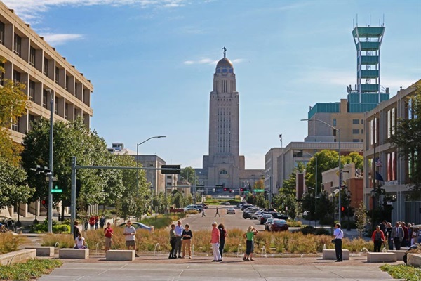 Community members enjoy the Centennial Mall pavilion with native grasses and water features on P St. Facing south down Centennial Mall, the Nebraska State Capitol Building stands tall over the center of the mall.
