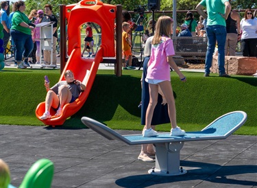 Teen standing on a teeter totter and another slides down a slide