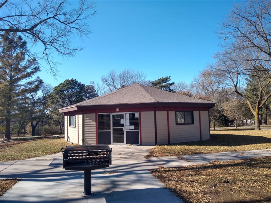 A picnic grill on a concrete pad is in front of the enclosed shelter inside Van Dorn Park.