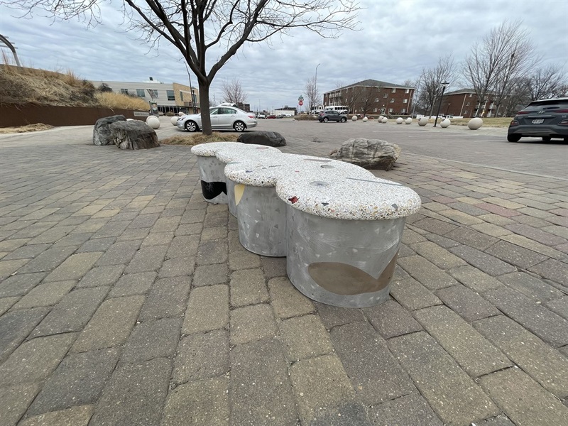 Round sides and a cloud shape top made of gray and colorful stone and glass make up this cloud bench