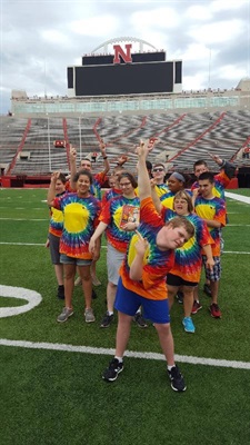 SumFun campers in their rainbow tie-dye camp shirts, raise their pointer fingers for #1 in Memorial Stadium.